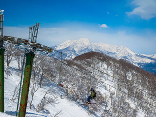 Single chair lifts in a ski resort and snowy peaks in a distant on a sunny day (Mt. Myoko, vired from Madarao Kogen, Nagano, Japan)