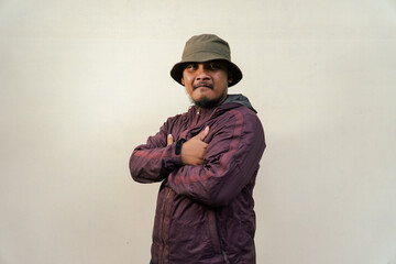 Half body portrait of mature Asian man with beard and mustache posing in ready style before traveling. Mature man wearing adventure outfit with jacket and bucket hat isolated on beige background.