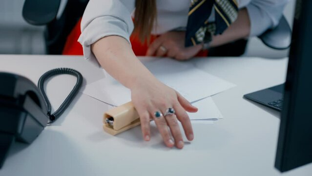 Close up of secretary's Hand using yellow office stapler to bind two papers together in slow motion. Woman wearing red skirt in office.
