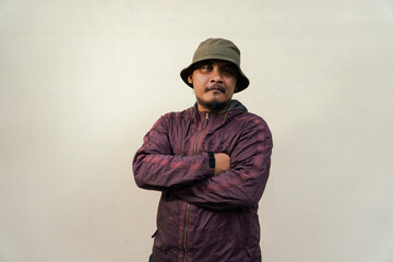 Half body portrait of mature Asian man with beard and mustache posing in ready style before traveling. Mature man wearing adventure outfit with jacket and bucket hat isolated on beige background.