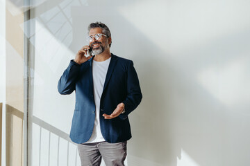 Mature business man smiling and talking on the phone by the balcony window