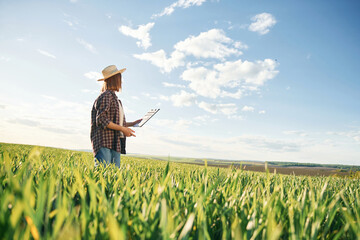 In straw hat and with documents. Young woman is on the beautiful agricultural field at daytime
