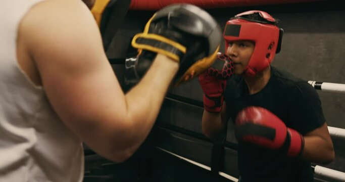 A teenager wearing a red protective helmet and gloves trains in a boxing ring with a coach.