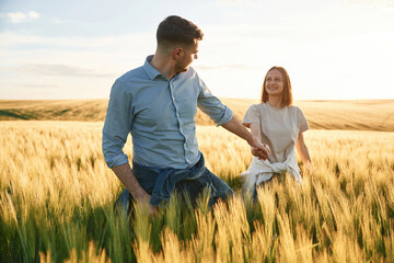 Leading the way, holding hands. Lovely beautiful couple are together on the agricultural field