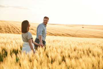 Leading the way, holding hands. Lovely beautiful couple are together on the agricultural field