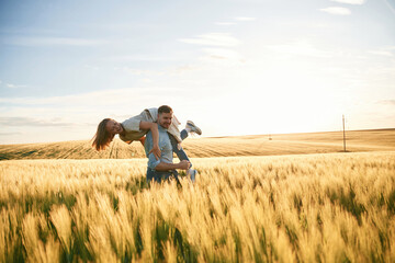 Having fun, man is holding woman. Lovely beautiful couple are together on the agricultural field