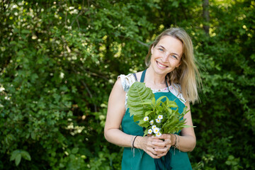 pretty, attractive woman in her early 40s, collects wild herbs in the garden, meadow, forest for a salad, for cooking, eating, for smoothies