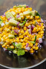  vibrant colors of a summer salad featuring corn, red onion, and avocado, drizzled with lime dressing, presented in a glass bowl in this closeup