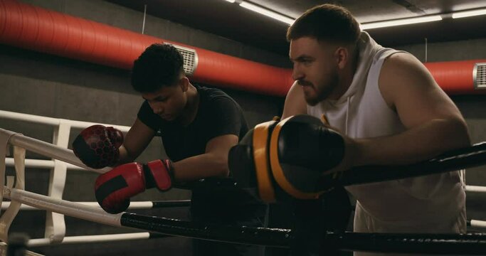Young Boxer Listens to Coach's Advice While Resting on the Ropes