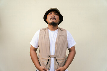 
Macho asian man with beard and mustache wearing safari clothes isolated on beige background. Half body portrait of an adult Southeast Asian man posing in many styles like an adventurer