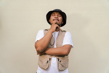 
Macho asian man with beard and mustache wearing safari clothes isolated on beige background. Half body portrait of an adult Southeast Asian man posing in many styles like an adventurer