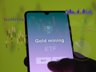 An investor analyzing the gold mining etf fund on a screen. A phone shows the prices of Gold mining