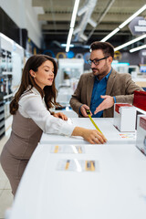 Beautiful and happy middle age couple buying consumer tech products in modern home appliances store. They are choosing washing or cloth dryer machine. People and consumerism concept.