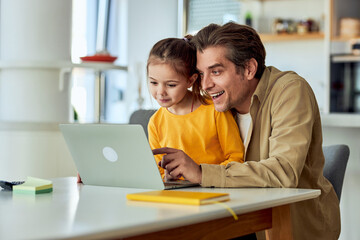 A happy father and his daughter watching a video online on a laptop at home