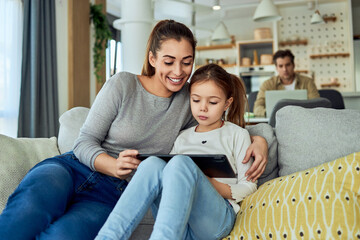 A happy mother and daughter watching a video on a tablet together while sitting on the couch in the living room