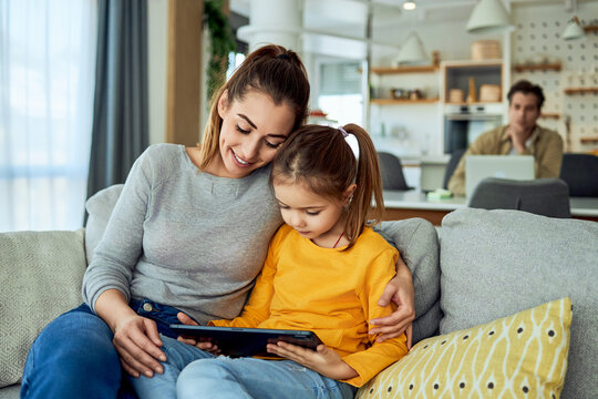 A mother and her daughter reading an online book on a digital tablet together while sitting on a couch