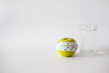 Green apple with white measurement tape and a glass of clean water. The concept of weight loss and...