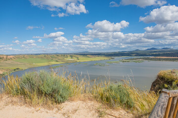 Panoramic view of the Burujón Canyon in Spain with the Tajo River and distant mountains under a vibrant blue sky with fluffy clouds.
The Tajo River meanders through the landscape, surrounded by green 