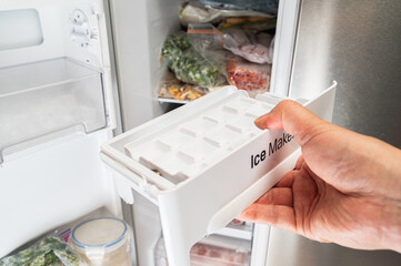 냉장고에 각얼음 제조기를 넣고 있는 남자의 손