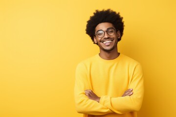 Portrait of a joyful afro-american man in his 20s with arms crossed while standing against pastel yellow background