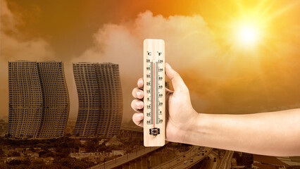 Human hand holding thermometer with hot temperature on the city