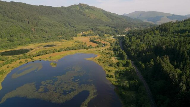 Aerial view of Loch Lubnaig surrounded by forest, mountains, and winding road, Highlands, United Kingdom.