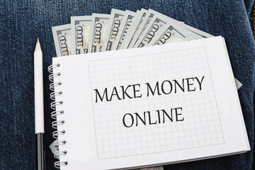 Business concept. MAKE MONEY ONLINE lettering written on a notebook lying on jeans with dollar bills