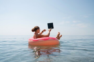 Woman laptop sea. Freelancer woman in sunglases floating on an inflatable big pink donut with a...