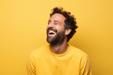 Portrait of a satisfied man in his 30s laughing on pastel yellow background