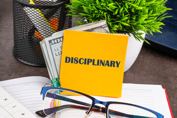 The concept of discipline or ethics word disciplinary written on a yellow sticker with dollars, on the desktop of a businessman, manager