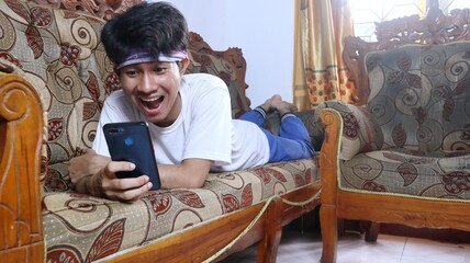 young Asian man lying on the sofa while using his smartphone