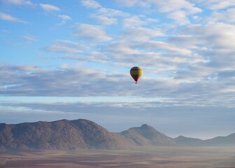 Brightly-colored hot air balloon soaring through the sky against a backdrop of distant mountains.