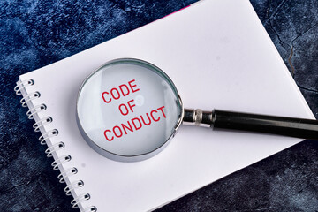 Business and code of conduct concept. Copy space. Code of conduct symbol written through a magnifying glass in a notebook on a beautiful blue heterogeneous background