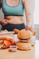 To eat or not. Cheerless plump woman looking at the burger while thinking to eat it or not