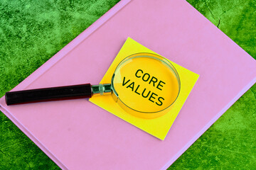 Copy space. Business and core values concept. The Core Values text through a magnifying glass on a yellow sticker lying on a business notebook on a green background