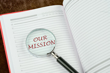 Our Mission symbol. Concept word Our Mission through a magnifying glass in the notebook of a businessman, manager, teacher