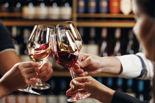 Big company people clinking glasses with red, rose and white wine on blurred cellar background. Men and women cheers with alcohol drink, closeup