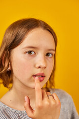 Naklejka premium A teenage schoolgirl with a contemplative look touches her lips against a vibrant yellow backdrop.