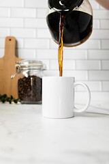 Person pouring hot, freshly brewed coffee from a pot into a mug sitting on a kitchen countertop.