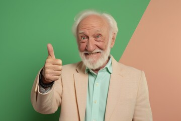 Portrait of a jovial man in his 80s showing a thumb up in front of solid pastel color wall
