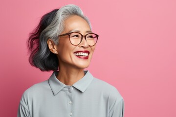 Portrait of a joyful asian woman in her 60s smiling at the camera while standing against solid...