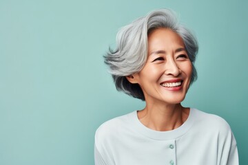 Portrait of a joyful asian woman in her 60s smiling at the camera isolated in solid pastel color...