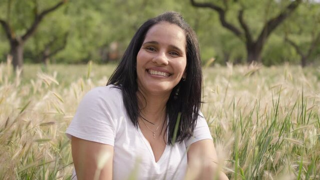 smiling beatiful woman seated in a tall grass field.MOV