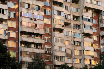The sunset reflecting in the many windows of a concrete, socialist, brutalist panel, multi-story,...