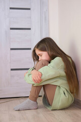 One sad girl sits on floor by door of the house. Child abuse. Anxiety and stress. Concept of...