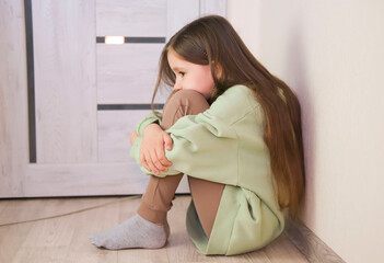 One sad girl sits on floor by door of the house. Child abuse. Anxiety and stress. Concept of...