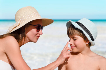 Woman carefully smears her child's face with protective cream on the beach. Skin care. Protection from the sun. Sunscreen for children.