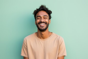 Fototapeta premium Portrait of a cheerful indian man in his 20s smiling at the camera over solid pastel color wall