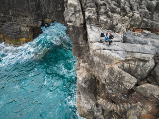A couple stands on a steep shore near the ocean. Boca do Inferno (Devil's Mouth) in Cascais is a...