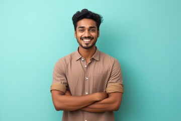 Portrait of a grinning indian man in his 20s with arms crossed isolated on solid pastel color wall